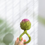 an adult's hand holding up a Oli & Carol Artichoke Rattle Teether
