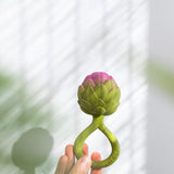 an adult's hand holding up a Oli & Carol Artichoke Rattle Teether
