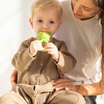 Child sitting on an adult's knee chewing an Oli & Carol Corn Rattle Teether toy