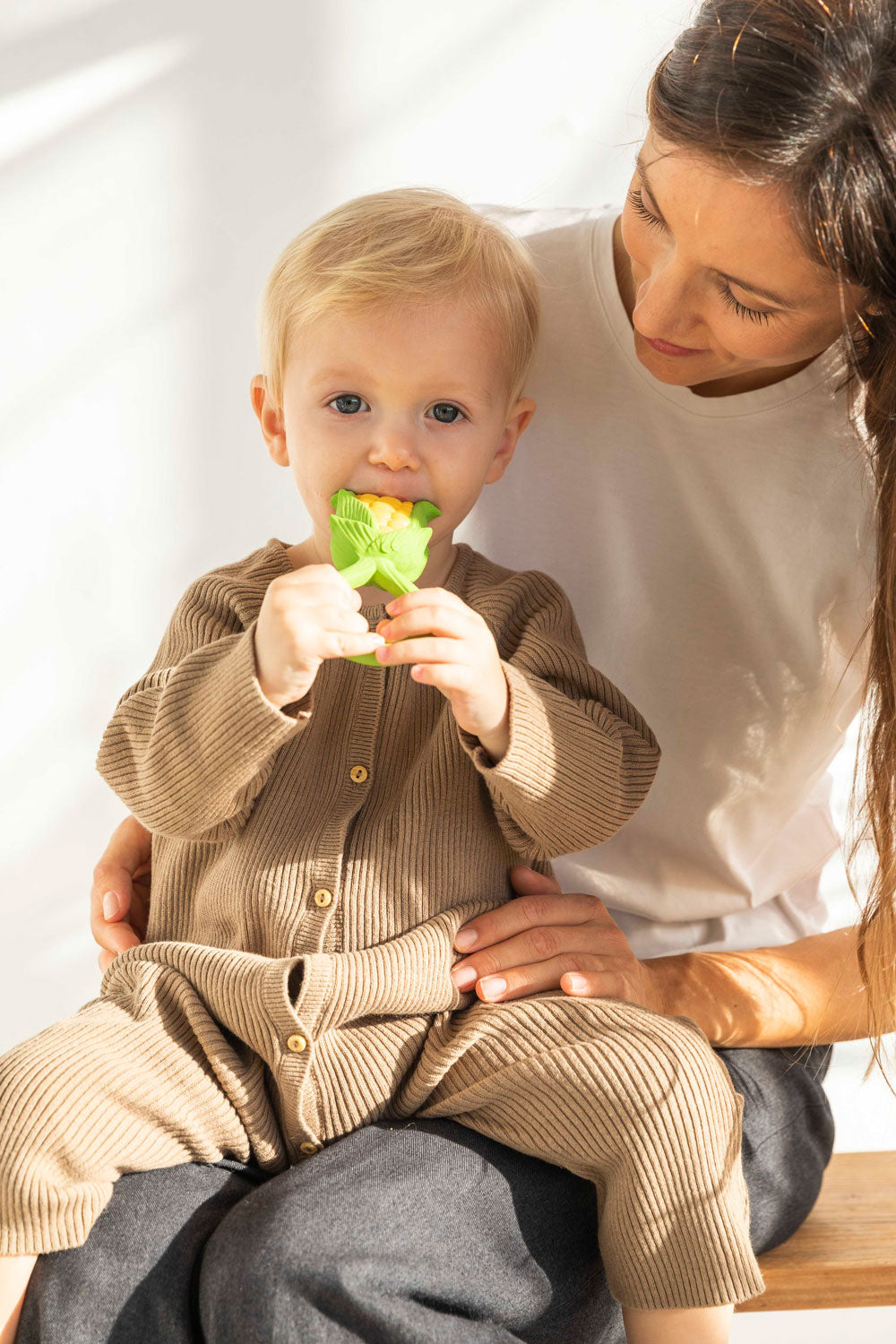 Child sitting on an adult's knee chewing an Oli & Carol Corn Rattle Teether toy