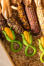 Oli & Carol Corn Rattle Teethers pictured on hat with real corn next to them