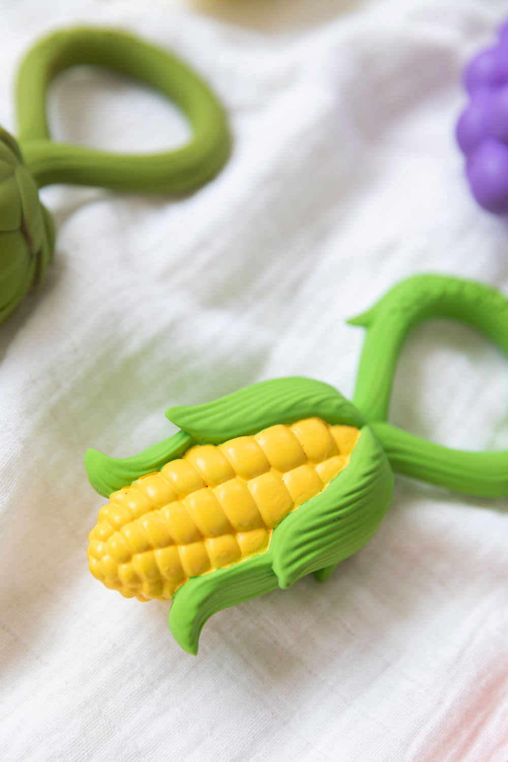 Oli & Carol Corn Rattle Teether placed on a white muslin cloth