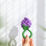 An adult's hand holding up the Oli & Carol Grape Rattle Teether
