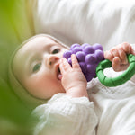 A baby clutching onto Oli & Carol Grape Rattle Teether