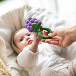 A baby reaching for an Oli & Carol Grape Rattle Teether