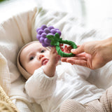 A baby reaching for an Oli & Carol Grape Rattle Teether
