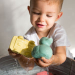 Child holding onto oli and carol yellow car and mint duck above a tub of water