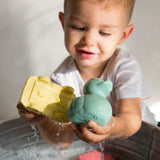 Child holding onto oli and carol yellow car and mint duck above a tub of water