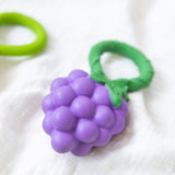 Oli & Carol Grape Rattle Teether pictured on a white muslin cloth