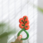 An adults hand holding up the Oli & Carol Tomato Rattle Teether toy