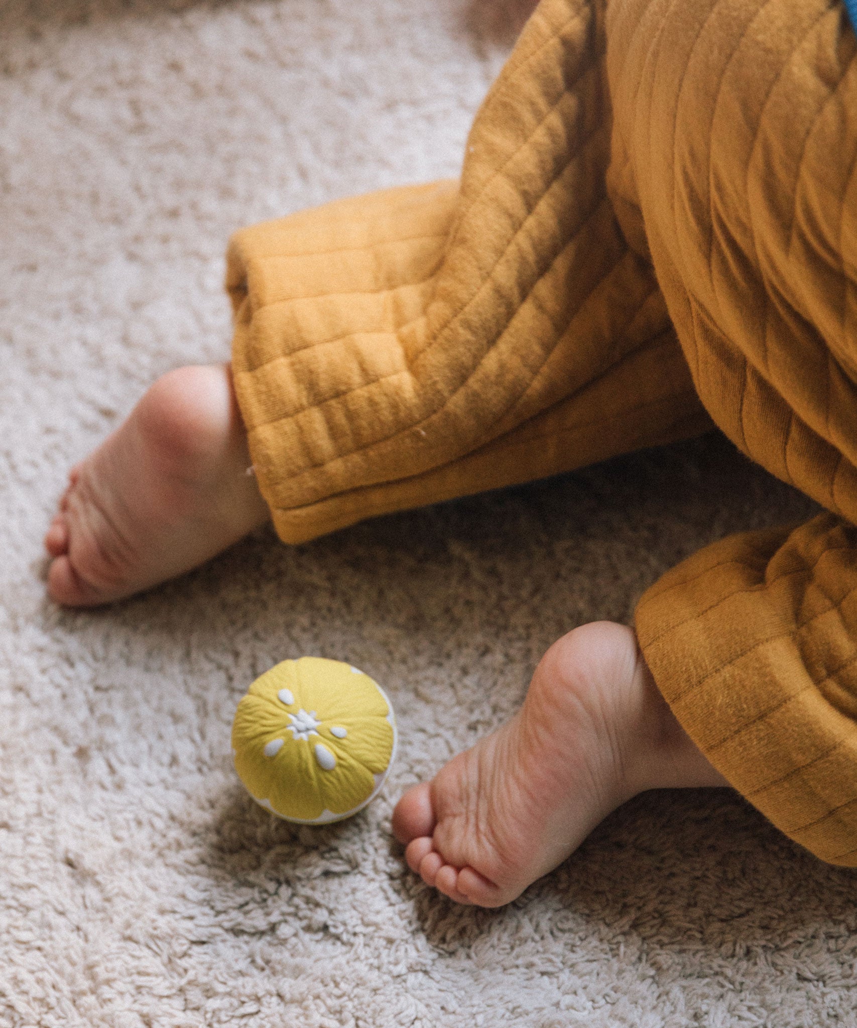 An Oli & Carol lemon baby sensory ball on carpet, a babies can be seen crawling away.