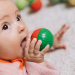 A baby holding onto a watermelon Oli & Carol sensory ball near their mouth