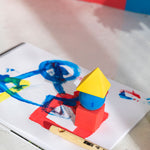 Oli & Carol X Bauhaus Movement Floating Geometric Blocks pictured on a sheet of painted paper