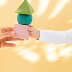 Oli & Carol X Bauhaus Movement Floating Geometric Blocks in Pastel colours stacked up being passed between adult and baby's hand