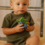 Close up of a child holding the oli and carol natural rubber baby teething toys on a cream blanket