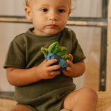 Close up of a child holding the oli and carol natural rubber baby teething toys on a cream blanket