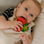 Close up of a toddler chewing on the oli and carol natural rubber raspberry teething toy
