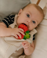Close up of a toddler chewing on the oli and carol natural rubber raspberry teething toy