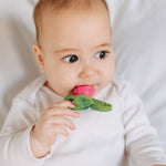 Close up of a baby chewing on the oli and carol ramonita radish teether on a white bed