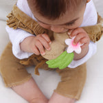 Close up of a toddler holding and chewing on the oli and carol aly the almond teething toy on a white blanket
