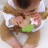 Close up of a toddler holding and chewing on the oli and carol aly the almond teething toy on a white blanket