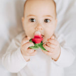 Close up of a baby chewing on the oli and carol eco-friendly radish teether on a white bed