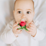 Close up of a baby chewing on the oli and carol eco-friendly radish teether on a white bed
