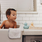 Chilb bathing in a large kitchen sink with Two oli & carol Elvis ducks on the counter top by their side