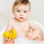 Baby in a small bath tub holding onto a yellow Oli & Carol Elvis The Duck Bath Toy