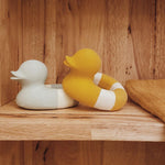 Yellow and mint coloured Oli & Carol Flo The Floatie Ducks placed on a wooden shelving unit