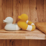 Yellow and mint coloured Oli & Carol Flo The Floatie Ducks placed on a wooden shelving unit