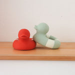 One Red and one mint coloured Oli & Carol Flo The Floatie ducks placed on a wooden shelf