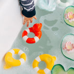 Child's hand reaching into a bath for the Oli & Carol Flo The Floatie Duck Red