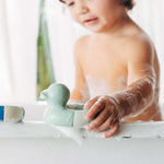 A child playing with the Oli & Carol Flo The Floatie Duck Mint in the bath. 