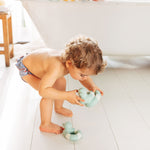 Child playing with the Oli & Carol Flo The Floatie Mint colour duck bath toys in a bathroom