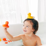Child holding a red Oli & Carol Flo The Floatie Duck in hand with a yellow one balanced on their head