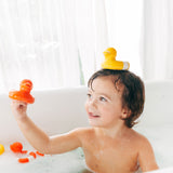 Child holding a red Oli & Carol Flo The Floatie Duck in hand with a yellow one balanced on their head
