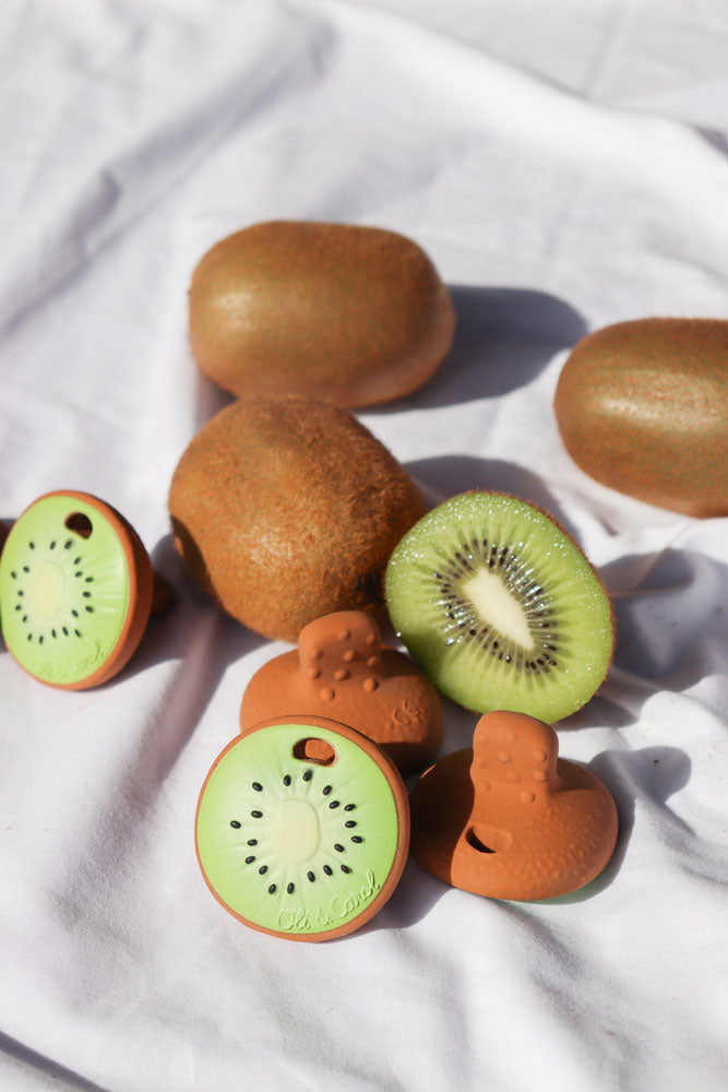 Oli & Carol Jose Antonio The Kiwi Mini Baby Teethers pictured amongst real kiwi fruit placed on a white cotton sheet