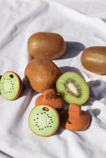 Oli & Carol Jose Antonio The Kiwi Mini Baby Teethers pictured amongst real kiwi fruit placed on a white cotton sheet