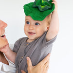 Woman holding a baby that is holding up the Oli & Carol mini kale baby comforter toy above its head