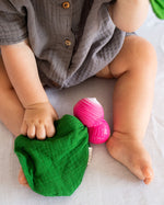Close up of the Oli & Carol eco-friendly mini radish baby comforter toy on a grey sheet next to a baby's leg