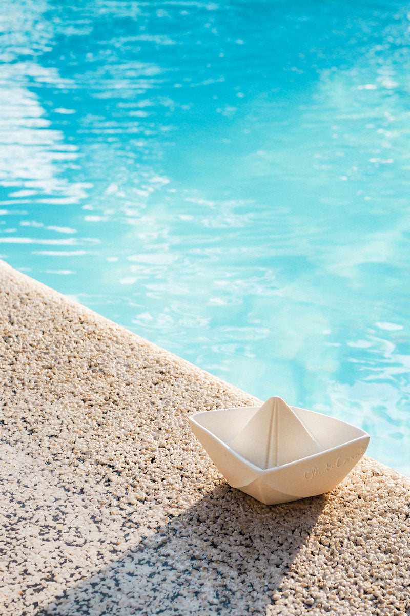 Oli & Carol White natural rubber Origami Boat bath toy pictured on the side of a pool