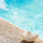Oli & Carol White natural rubber Origami Boat bath toy pictured on the side of a pool