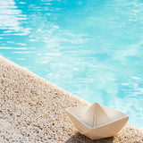 Oli & Carol White natural rubber Origami Boat bath toy pictured on the side of a pool