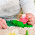 Close up of a baby's hand grasping the oli and carol natural rubber radish teething toy on a white carpet