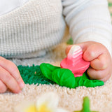 Close up of a baby's hand grasping the oli and carol natural rubber radish teething toy on a white carpet