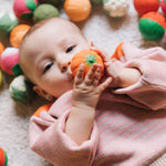 A baby grasping onto the pumpkin ball from the Oli & Carol Vegetable soup Baby Sensory Balls set