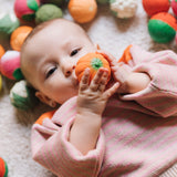 A baby grasping onto the pumpkin ball from the Oli & Carol Vegetable soup Baby Sensory Balls set