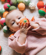A baby grasping onto the pumpkin ball from the Oli & Carol Vegetable soup Baby Sensory Balls set