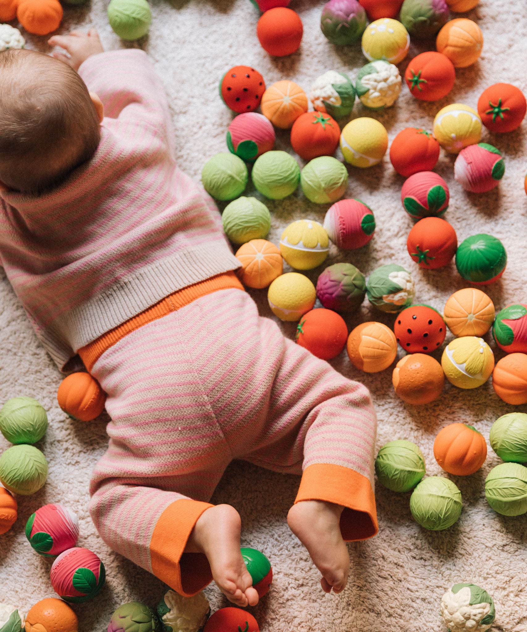 A baby laying on their front surrounded by Oli& Carol baby sensory balls